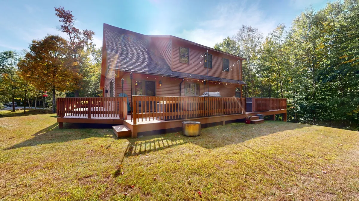 This exterior shot captures the wooden deck, framed by mature trees and the exterior of the house. The scene evokes a sense of privacy and immersion in nature, inviting guests to step outside for gatherings or quiet moments. The vantage point emphasizes the spaciousness of the deck and its harmony with the wooded landscape.