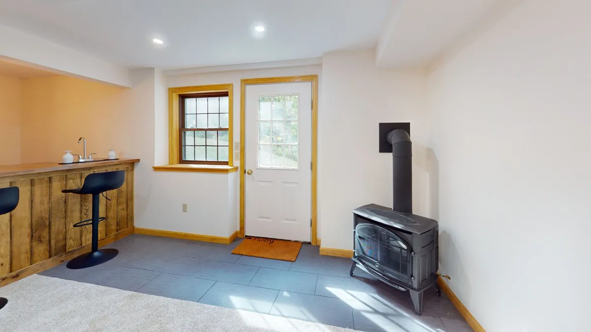 A cozy bar area with a wooden stove and windows that draw in morning light. The bar area’s open feel hints at easy transitions between interior and exterior relaxation, supporting socializing and entertaining.
