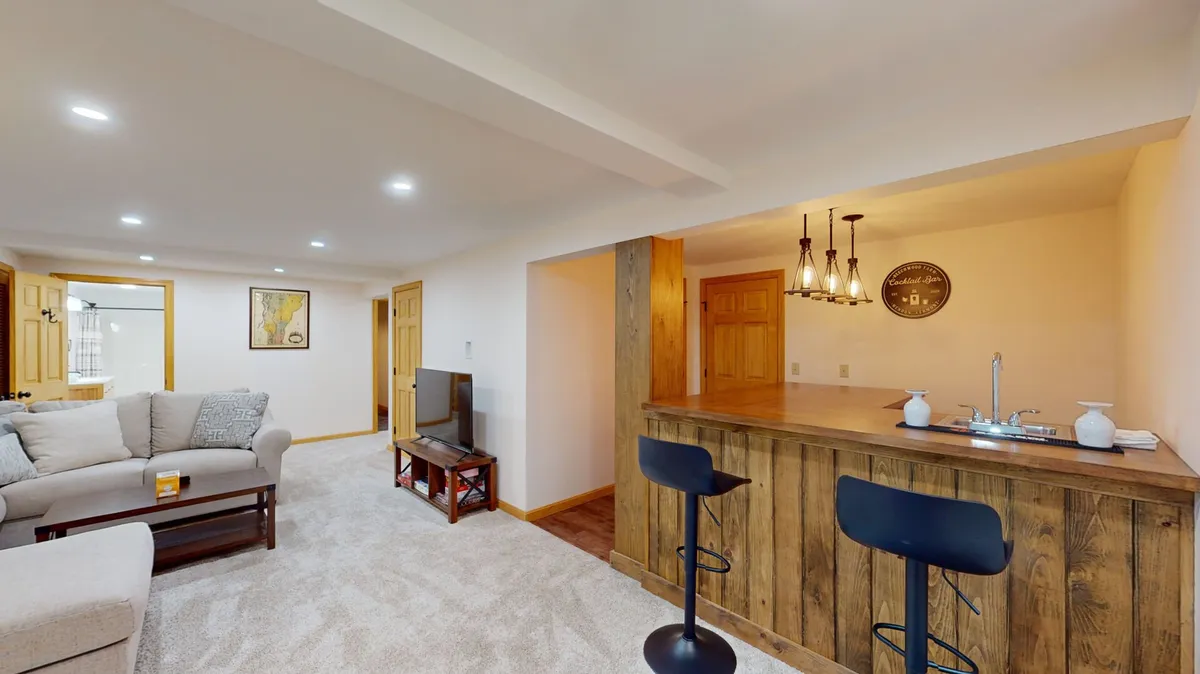 A cozy entertainment area with a home bar equipped with stools, a comfortable sofa, and a television. The inviting bar area sets the scene for socializing and relaxing, ideal for family or group activities.