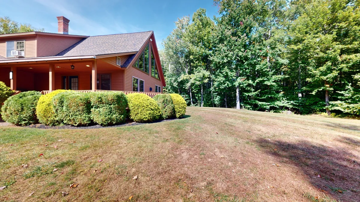 A view of the house's facade set against a landscaped garden and encircled by mature trees. This image highlights the home's harmonious relationship with its wooded environment, hinting at private woodland explorations and seasonal changes visible from the property.