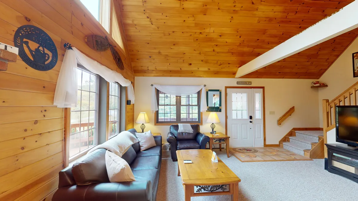 A cozy living room setting with a leather sofa, wooden coffee table, and expansive windows flooding the space with natural light. The room is perfect for relaxing, socializing, or enjoying peaceful moments indoors.