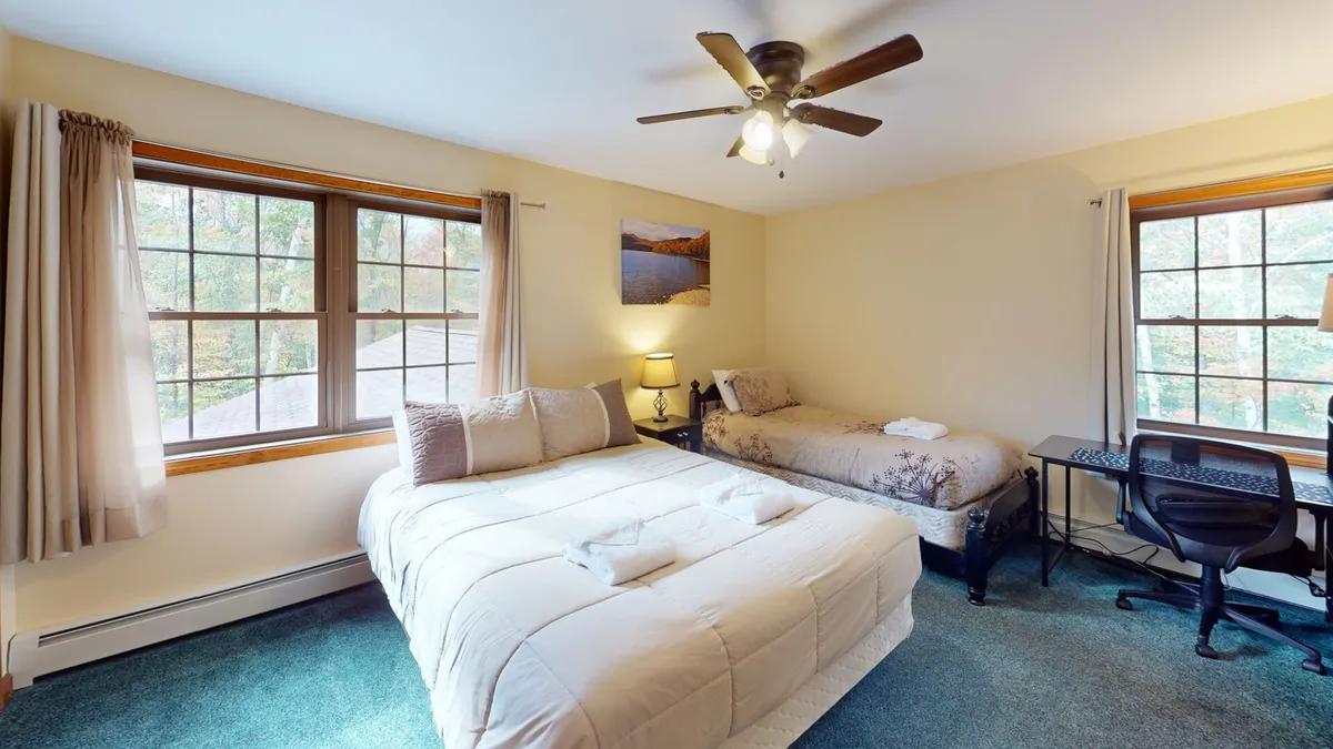 A tranquil bedroom combining a large bed, single bed, a desk with a chair, and a window revealing calming nature views. The room is softly lit, offering a restful, private sanctuary for relaxation or quiet activities like reading.